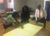 Three people are standing around a table with a large sheet of paper.