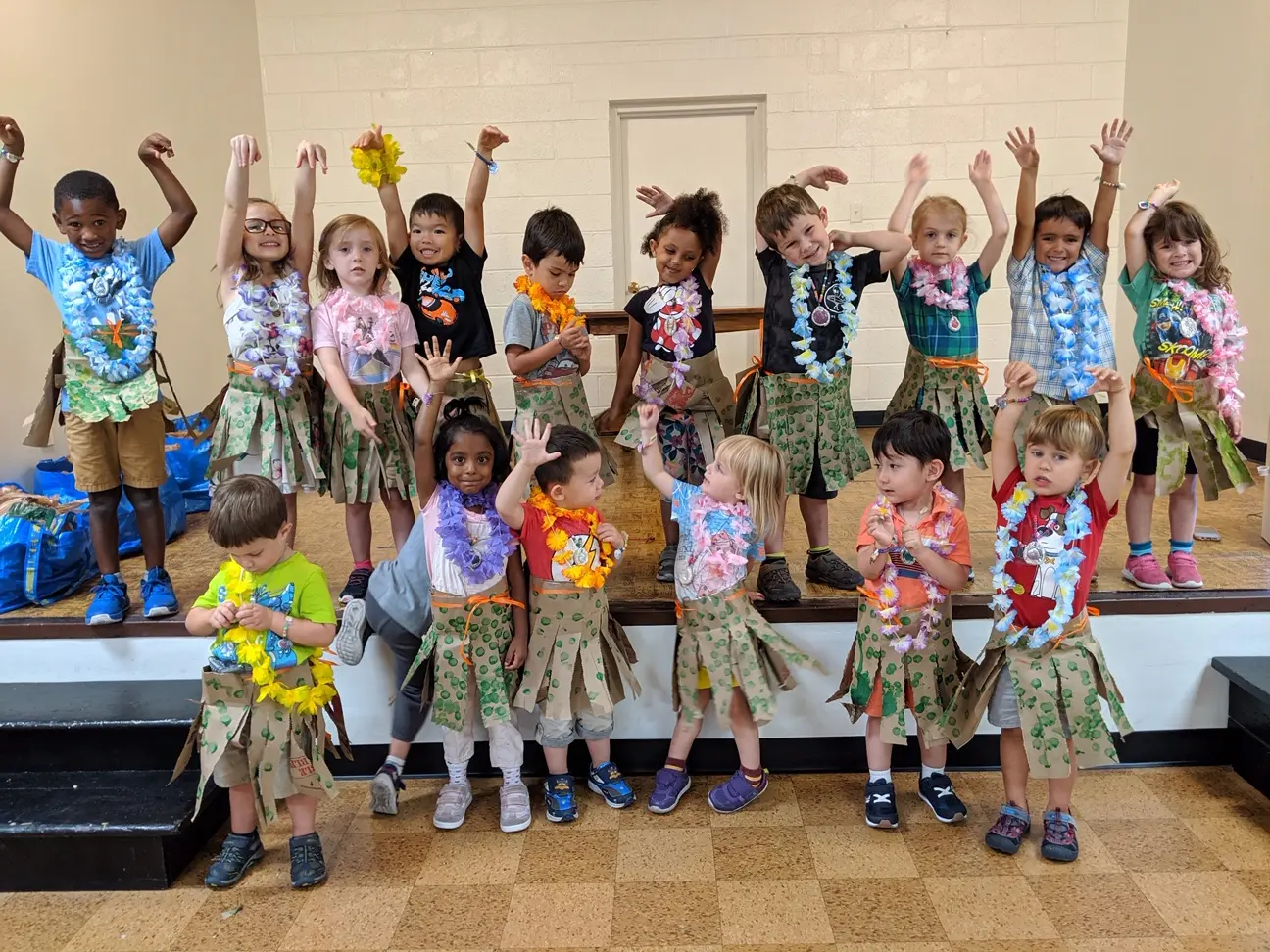 A group of children in hawaiian shirts and grass skirts.