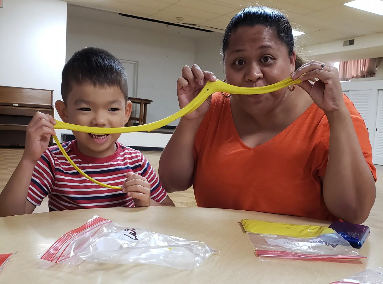 A woman and boy holding yellow string around their mouth.