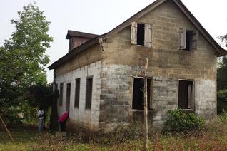 A dilapidated house with no windows and a tree in the background.