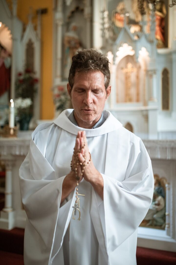 A man in white robe holding his hands together.